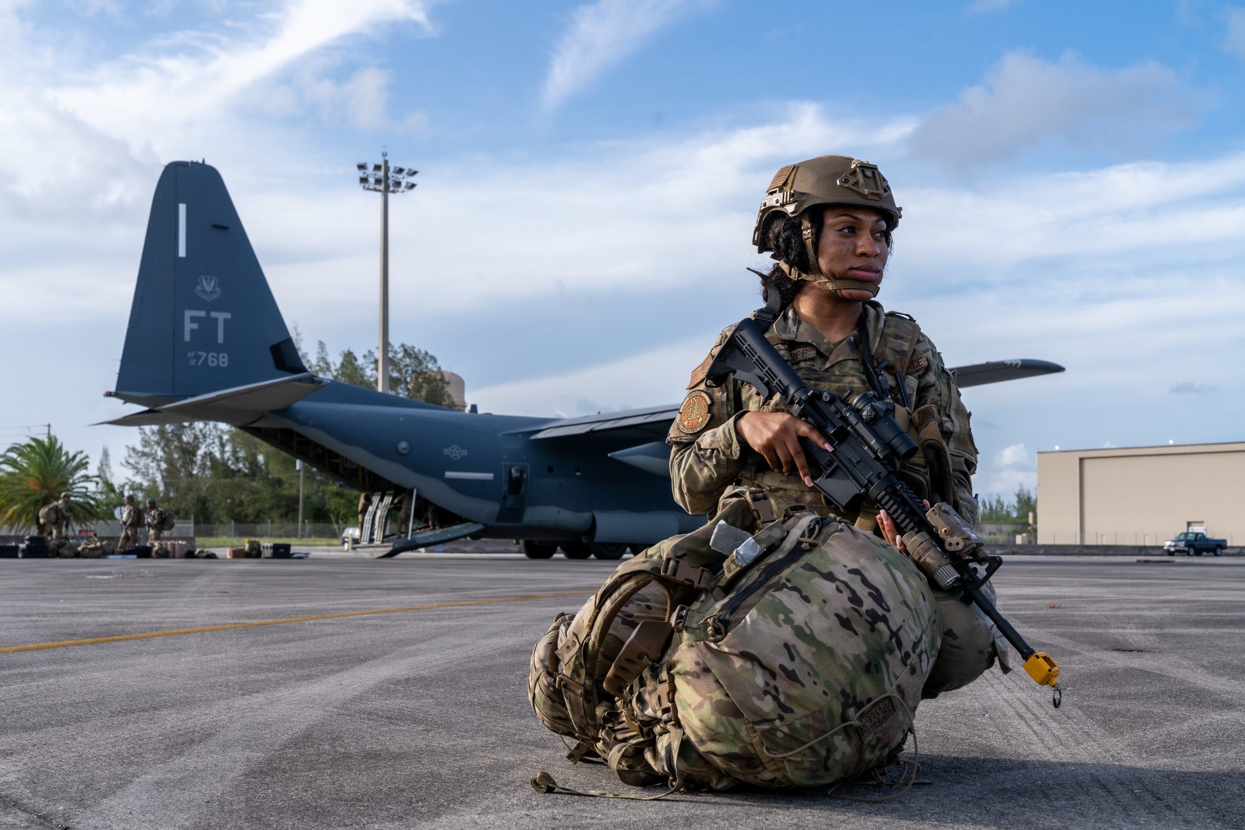 individual holding a rifle kneeling in front of a plane